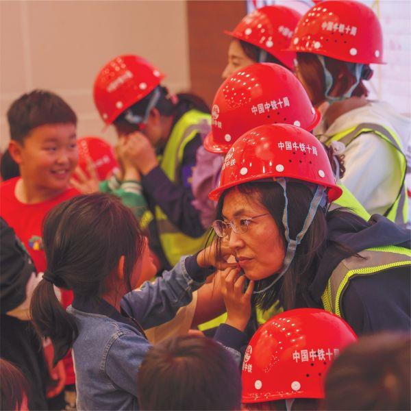 六一 5月29日，在中铁十局一公司安全讲解员的带领下，来自公司近二十组家庭的萌娃们化身小小“安全员”，与父母共同参与了在遥墙机场项目部开展的“萌娃进工地，童声嘱安全”亲子活动。图为孩子们为爸爸妈妈佩戴安全帽。